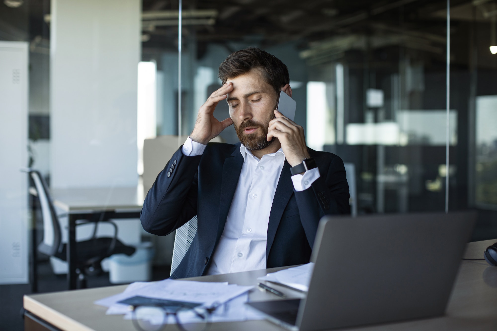 Concerned male entrepreneur talking on cellphone and touching head in stress, having unpleasant
